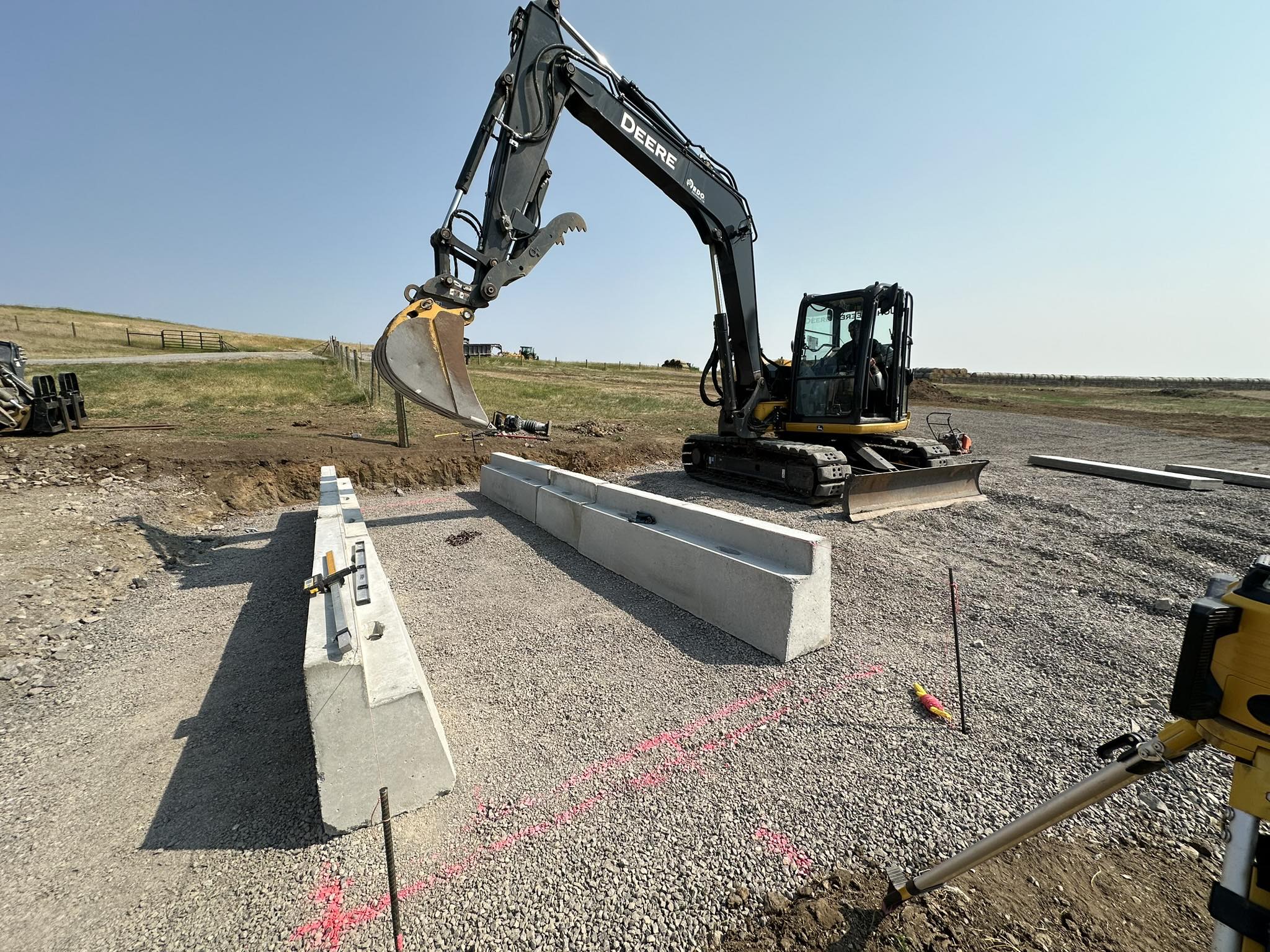 Excavator setting concrete blocks on gravel lot under a clear sky at a rural job site