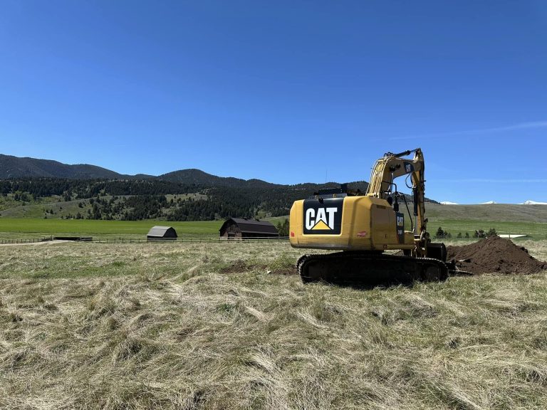 Yellow CAT excavator digging into a large open field during landscape and irrigation setup in Montana