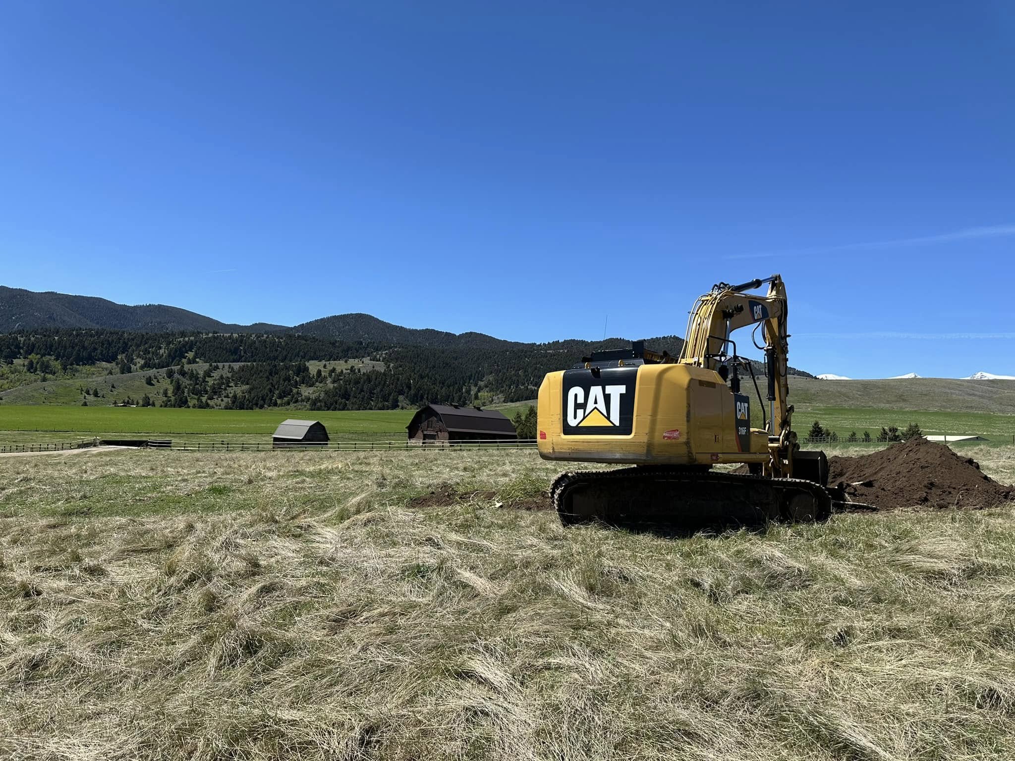 Yellow CAT excavator digging into a large open field during landscape and irrigation setup in Montana