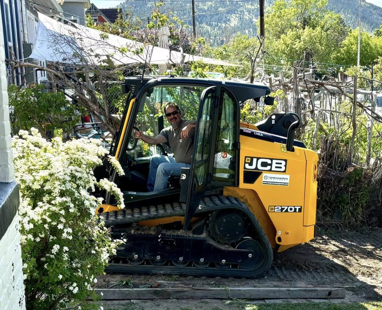 Smiling equipment operator inside JCB 270T compact track loader at Butte MT residential excavation site