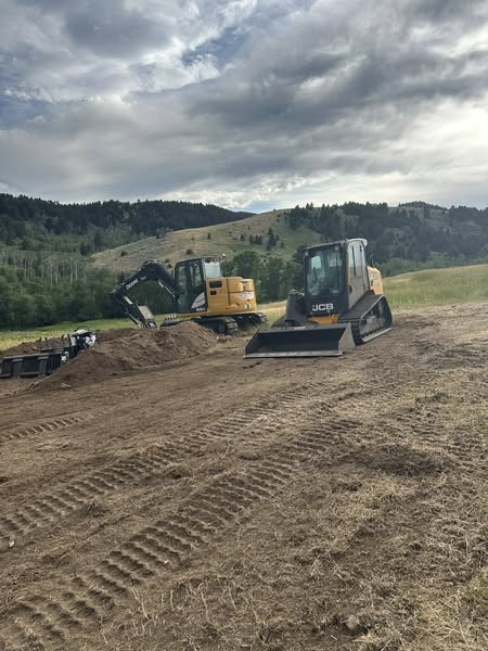 JCB loader and excavator working on land clearing and site preparation in a hilly Montana landscape