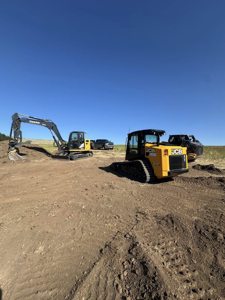 Yellow and black heavy machinery parked on a level dirt site under a clear blue sky