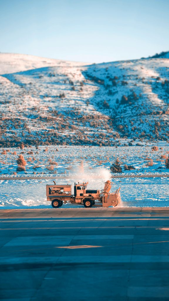 Snowplow truck clearing snow from a road with snow-covered hills in the background