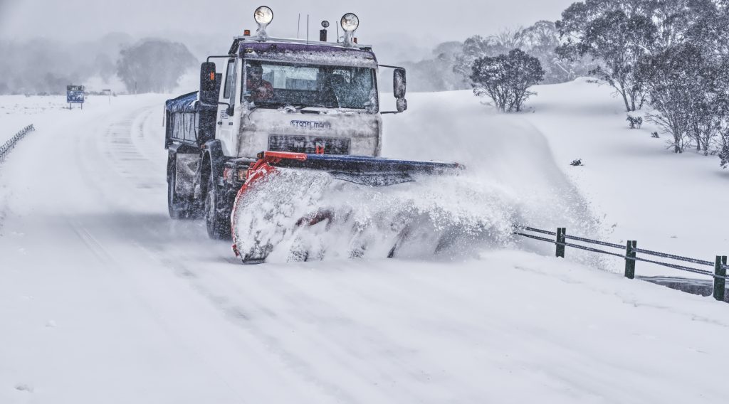 A powerful snowplow truck pushes thick snow off a rural Montana road, restoring accessibility after heavy snowfall.